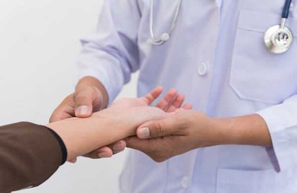 Doctor examining hand of patient while the patient has pain and old surgical wound
