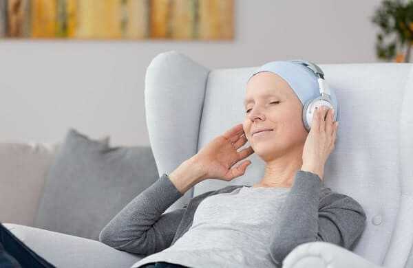 Woman with cancer listening to music on headphones at home