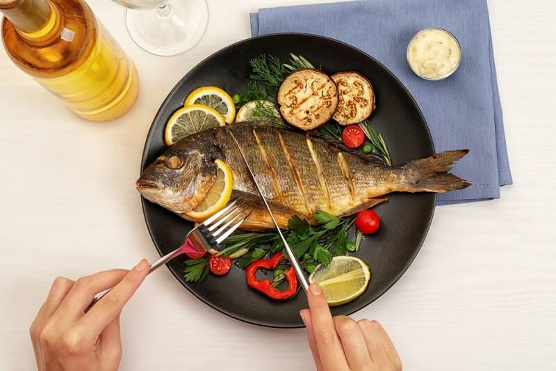 Female hands cutting tasty fish on plate