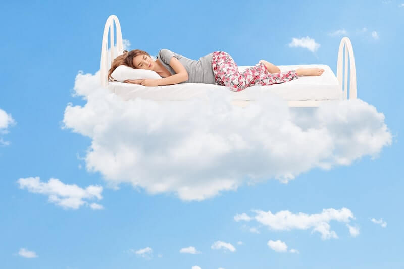 Relaxed young woman sleeping on a comfortable bed in the clouds