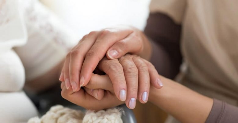 a female caregiver and senior woman holding hands