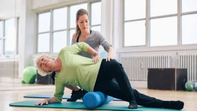 Female instructor helping senior woman using a foam roller for a myofascial release massage at gym