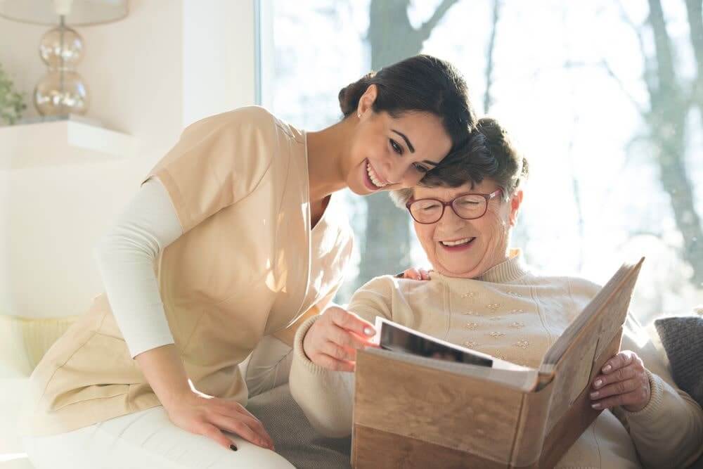 Smiling senior woman watching photo album with happy caregiver