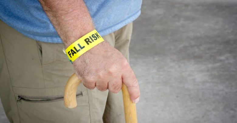 Fall risk bracelet around an elderly man's wrist while walking with a wooden cane